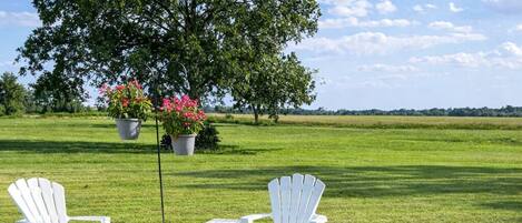 A stone fire pit surrounded by white chairs and a table in a grassy field.