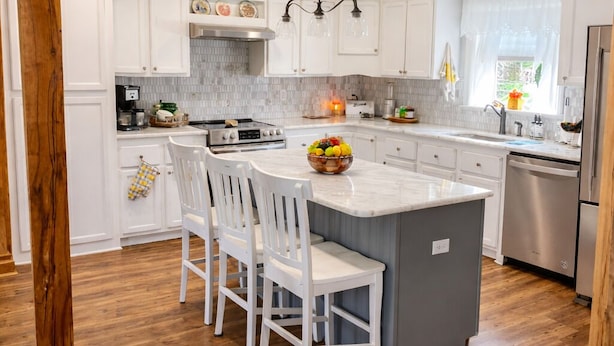 A kitchen with white cabinets, a central island with chairs, a stainless steel refrigerator, and a wooden ceiling structure. - Amazing 3-bedroom home in charming O'Brien Florida (O'Brien)