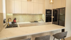 A modern kitchen with a large island, bar stools, a built-in oven, and a black refrigerator. - Villa Elysium (Petrovac)
