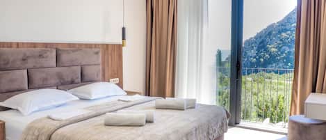 A hotel room with a bed, a bedside table, a window with curtains, and a view of a mountain.