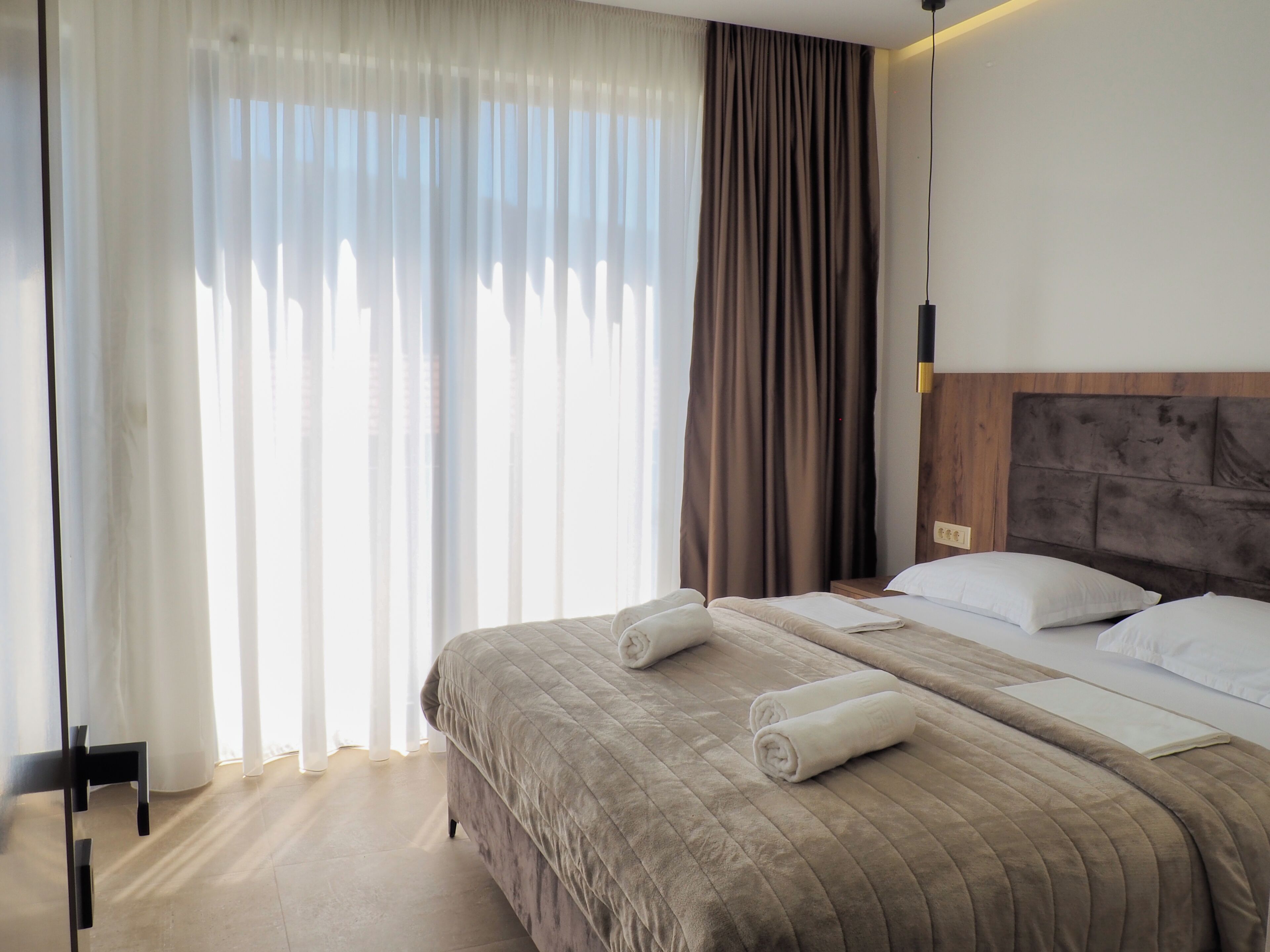 Ein Hotelzimmer mit einem großen Bett, einem hölzernen Kopfteil und Blick durch transparente Vorhänge.