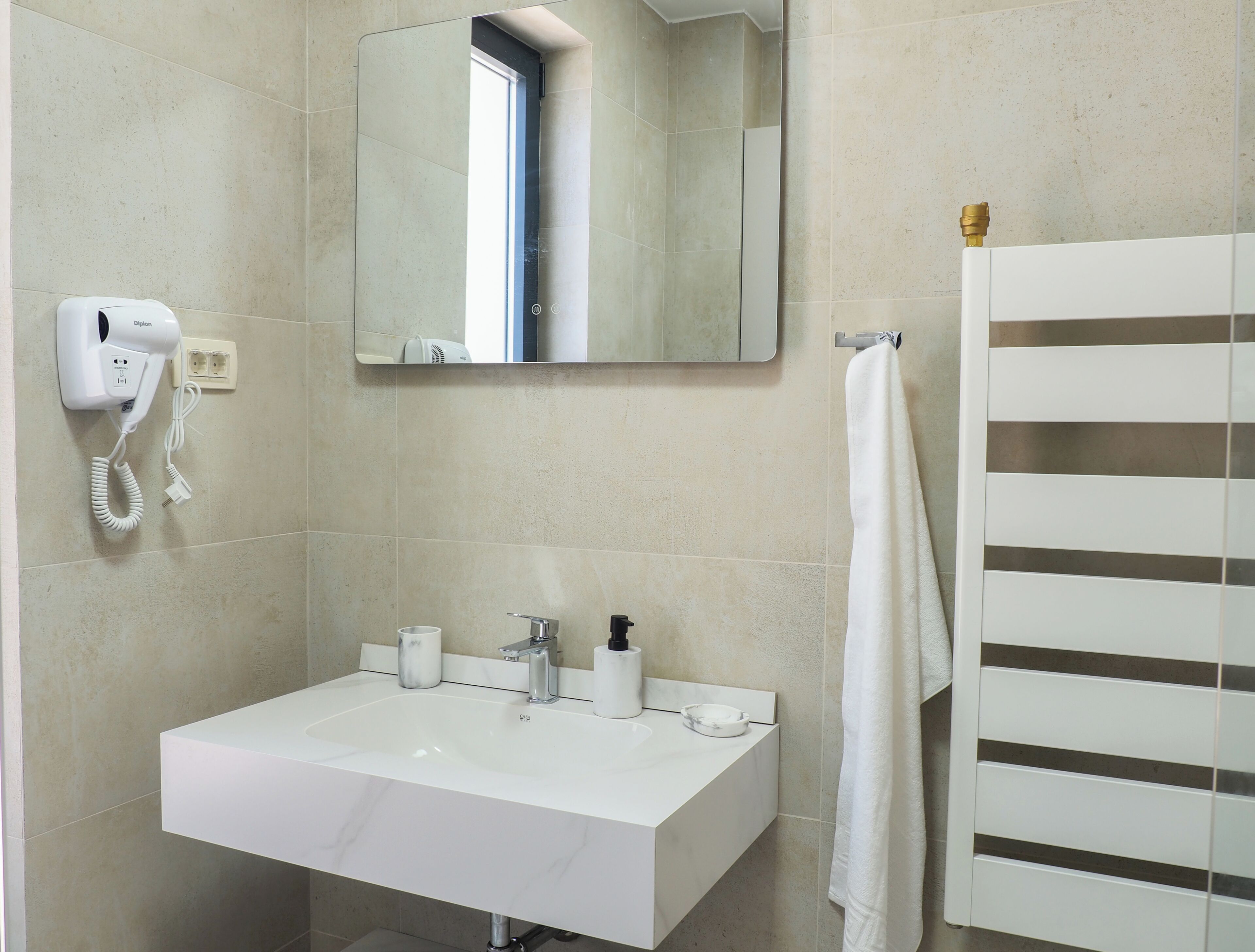 A bathroom with a white sink, a mirror, a hairdryer, and a towel rack.