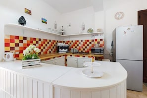 Une cuisine avec un dosseret à carreaux, des meubles blancs, un réfrigérateur et un four à micro-ondes.