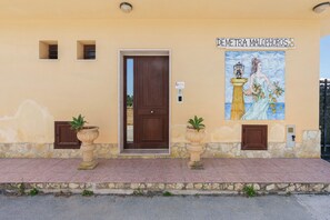 Un edificio con una porta in legno, due piante in vaso, un mosaico in maiolica e un muro in pietra.