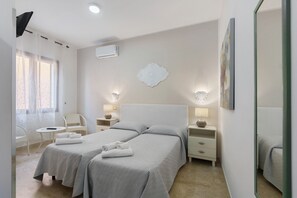 Une chambre d’hôtel avec deux lits, une petite table, des chaises, des lampes de chevet, un appareil de climatisation et un élément décoratif mural.