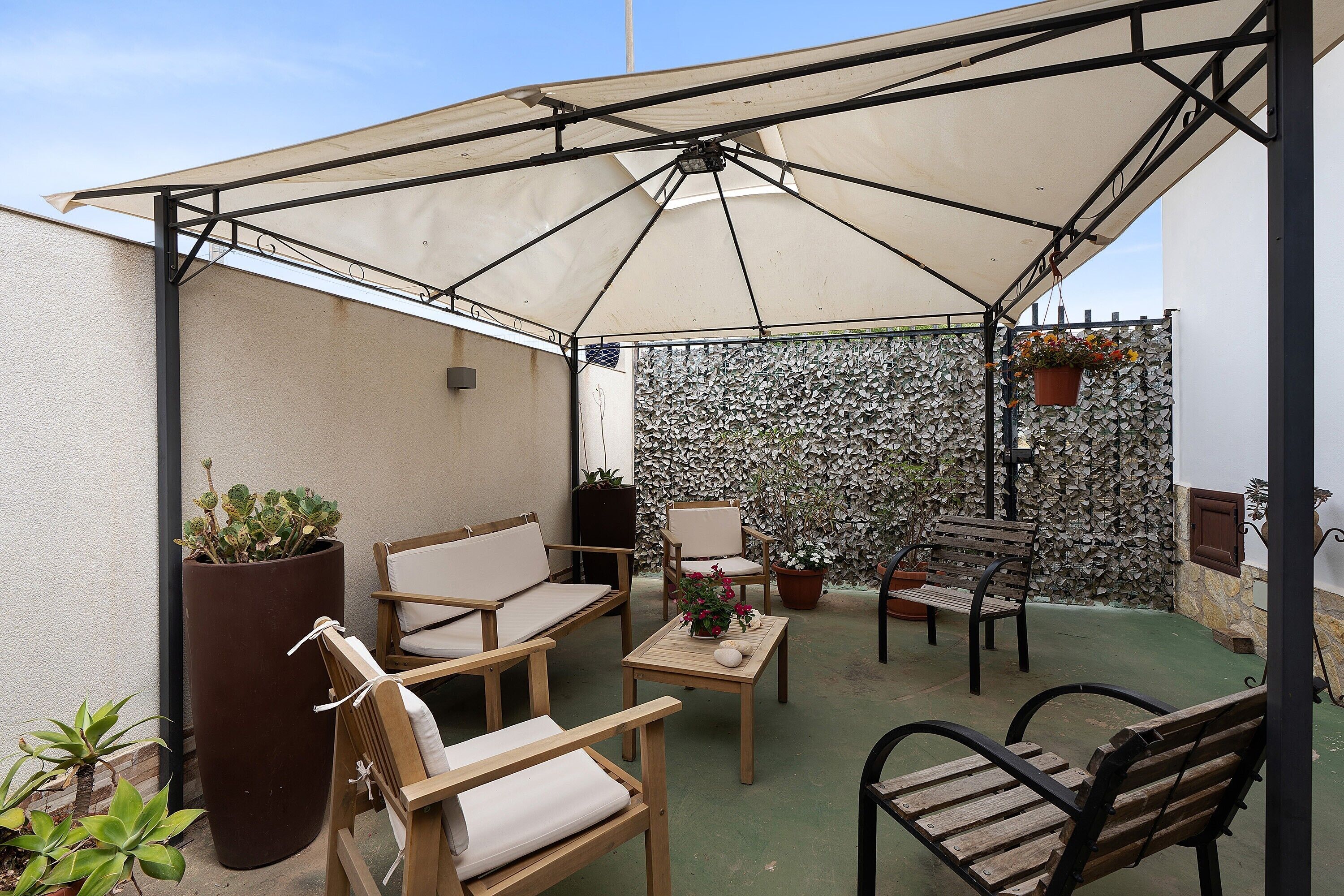 A covered patio area with seating, potted plants, and a decorative wall.