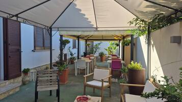 Un patio al aire libre con mesas, sillas, plantas en macetas y una sección cubierta.