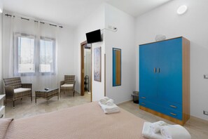 Une chambre à coucher comprenant un lit, deux chaises, une armoire, un téléviseur et une salle de bain visible à travers une porte ouverte.