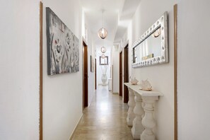 Un couloir avec un mur blanc, un grand miroir, un vase et un tableau.