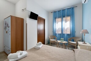 Une chambre à coucher comprenant un lit, deux fauteuils en osier, une petite table, un téléviseur, une armoire et une fenêtre avec un rideau.