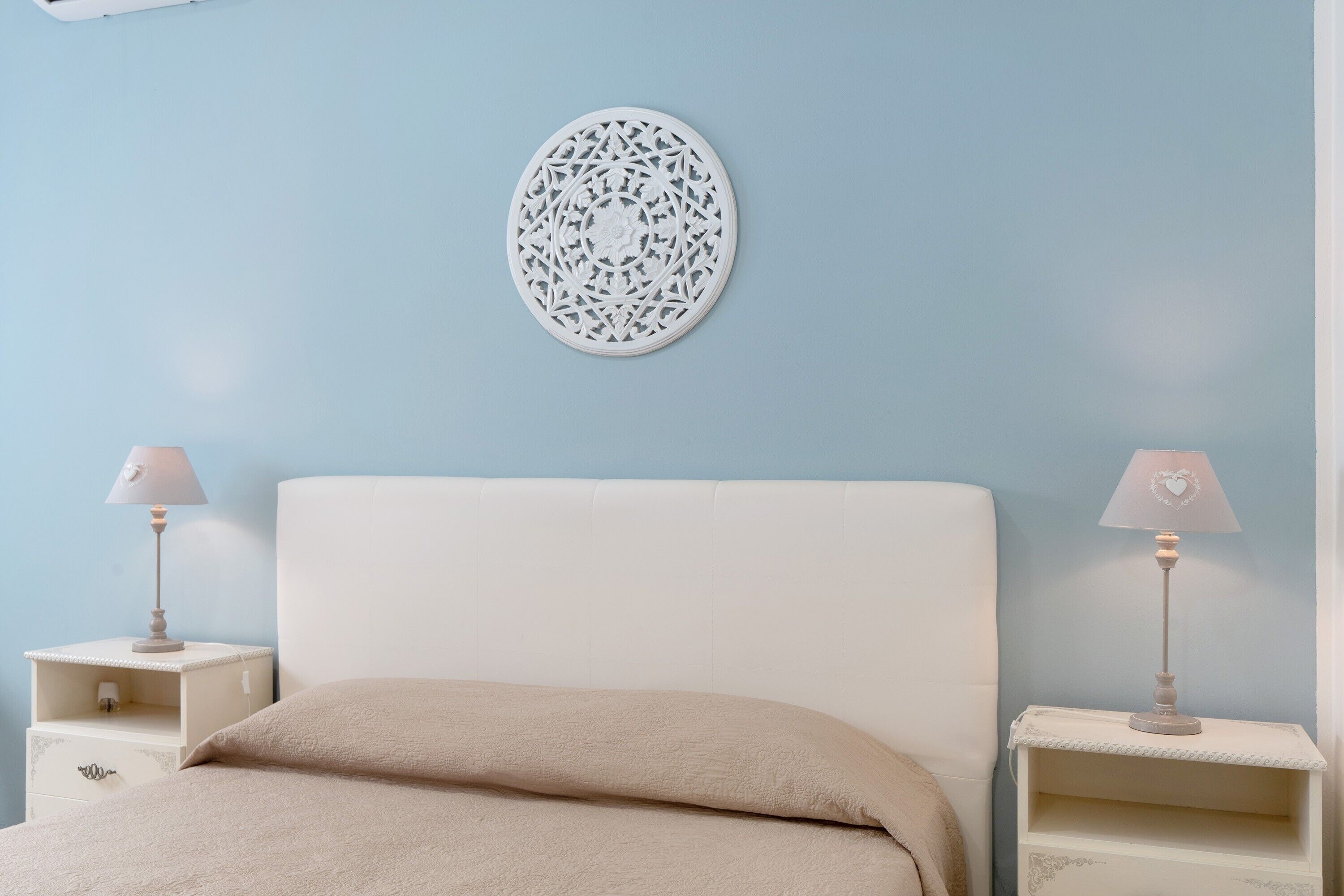 Une chambre à coucher comprenant un lit, deux tables de chevet, un élément décoratif fixé au mur et une petite table de nuit avec une lampe.