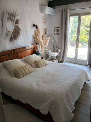 A bedroom with a large bed, a white chair, an air conditioning unit, and a view of the outdoors. - Charming house in the Var in a residence with swimming pool (Seillans)