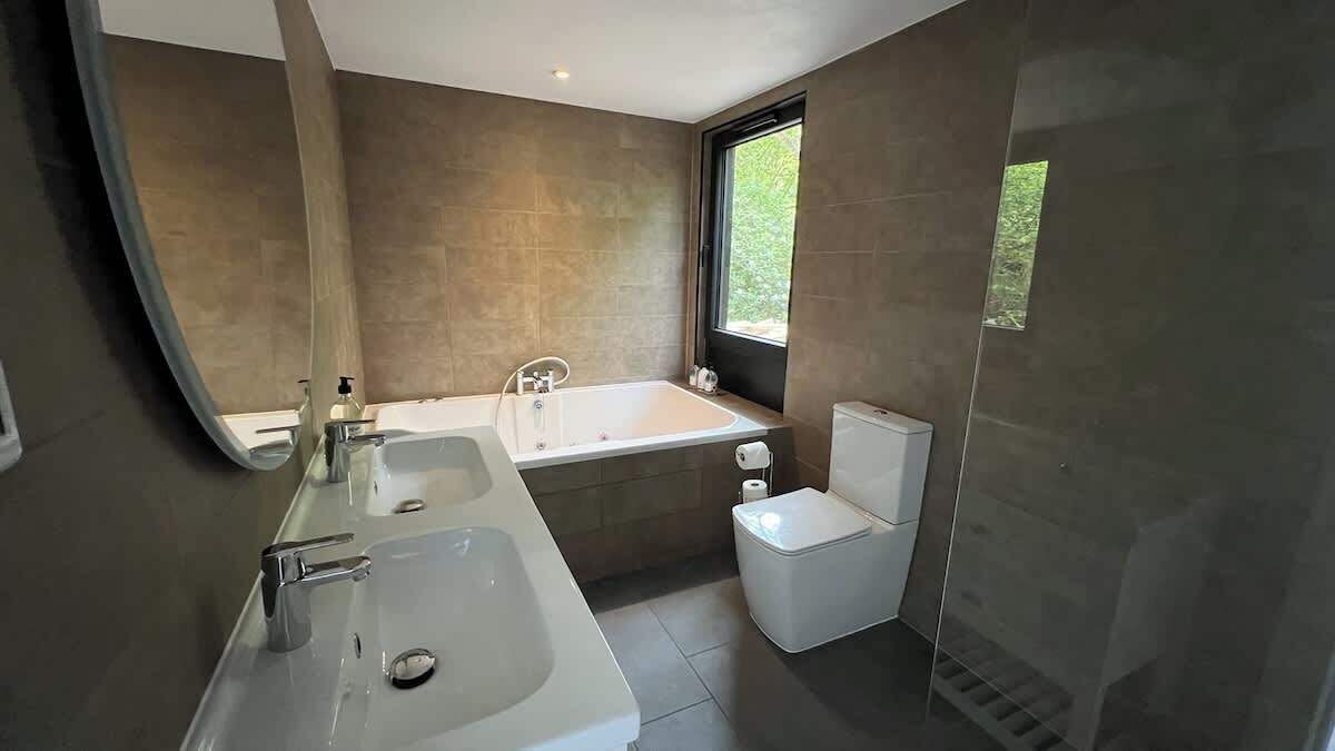 A modern bathroom with a bathtub, two sinks, and a toilet.