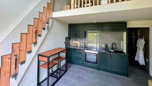 A modern kitchen with dark green cabinets, a wooden staircase, and a small dining area.