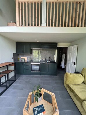 Una cocina moderna con armarios oscuros, horno empotrado y comedor con mesa y sillas de madera.
