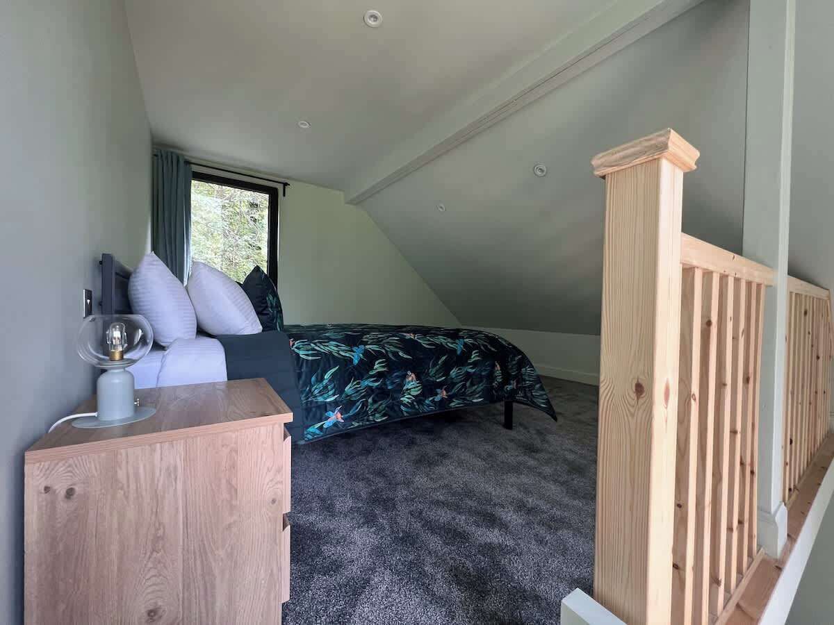 Un dormitorio con cama, una mesita de noche con lámpara, una ventana y un panel de madera.