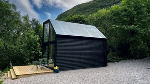 A modern cabin with a sloped roof, a glass door, and a small deck area.