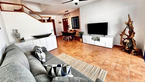 Een moderne woonkamer met een bank, televisie, houten trap, eethoek en een decoratieve boomsculptuur.