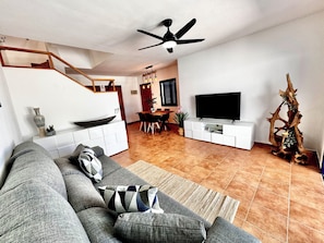 Ein modernes Wohnzimmer mit Sofa, Fernseher, einer Holztreppe, Essbereich und einer dekorativen Baumskulptur.