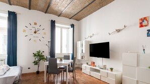 A modern room with a dining area, a flat-screen TV, a clock, and a potted plant. - Lovely 1-bedroom apartment with AC in vibrant Roma (Roma)