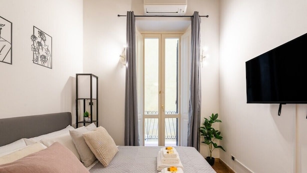 A bedroom with a bed, a TV, a window with curtains, and a plant. - Lovely 1-bedroom apartment with AC in vibrant Roma (Roma)