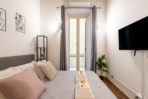 Ein Schlafzimmer mit einem Bett, einem Fernseher, einem Fenster mit Vorhängen und einer Pflanze.