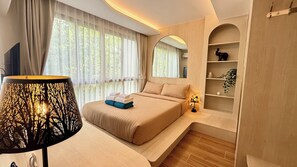 A modern hotel room with a bed, bedside lamp, and a shelf with decorative items. - All You Need in Kamala | Rooftop Pool + Gym + Shuttle A613 (Tambon Kamala)