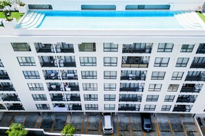 A multi-story hotel with balconies, a rooftop pool, and a parking area. - All You Need in Kamala | Rooftop Pool + Gym + Shuttle A613 (Tambon Kamala)