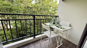 A balcony with a white table and chairs, a potted plant, and a view of trees. - All You Need in Kamala | Rooftop Pool + Gym + Shuttle A613 (Tambon Kamala)