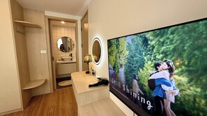A modern bathroom with a vanity, mirror, and a large TV screen displaying a nature scene. - All You Need in Kamala | Rooftop Pool + Gym + Shuttle A613 (Tambon Kamala)