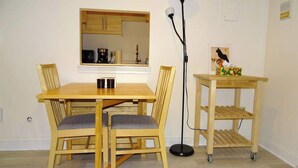 A dining area with a wooden table and chairs, a floor lamp, and a small cart with a cat figurine.