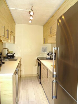 A modern kitchen with stainless steel appliances, wooden cabinets, and a light-colored floor.