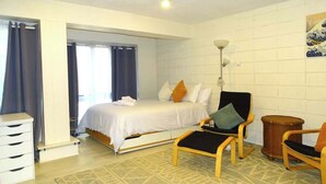 A bedroom with a bed, two chairs, a small table, a dresser, and a patterned rug.