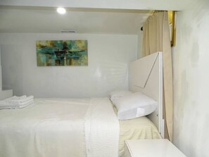 A neatly made bed with white linens, a painting on the wall, and a window with curtains. - Cozy 1 Bed Apt in Randolph (Randolph)