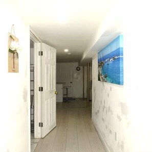 A hallway with a white door, a painting of a coastal scene, and a small table with a stool. - Cozy 1 Bed Apt in Randolph (Randolph)