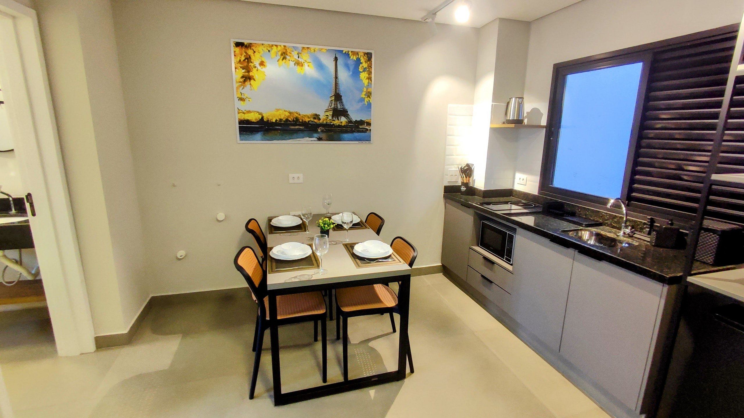 A dining area with a table set for four, a kitchen with modern appliances, and a painting of the Eiffel Tower on the wall.
