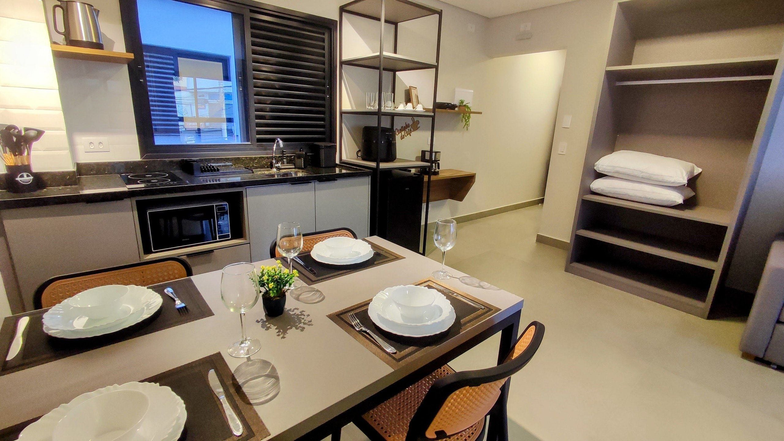 Una cocina compacta con electrodomésticos modernos, un comedor con una mesa dispuesta para dos personas y un mueble de estanterías empotrado.