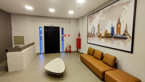 A reception area with a desk, a couch, a fire extinguisher, and a world map mural. - Airport Residence (Guarulhos)