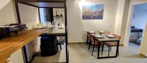 A compact kitchen with a coffee machine, a dining area with a table set for four, and a painting of a cityscape on the wall.