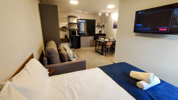 Ett hotellrum med en säng, en soffa, en TV, ett litet kök och en matplats.