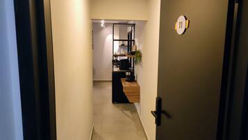 A hallway leading to a room with a desk, a shelf with items, and a door with a number plaque.