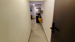 A narrow hallway leading to a room with a desk, chair, and a small plant. - Airport Residence (Guarulhos)