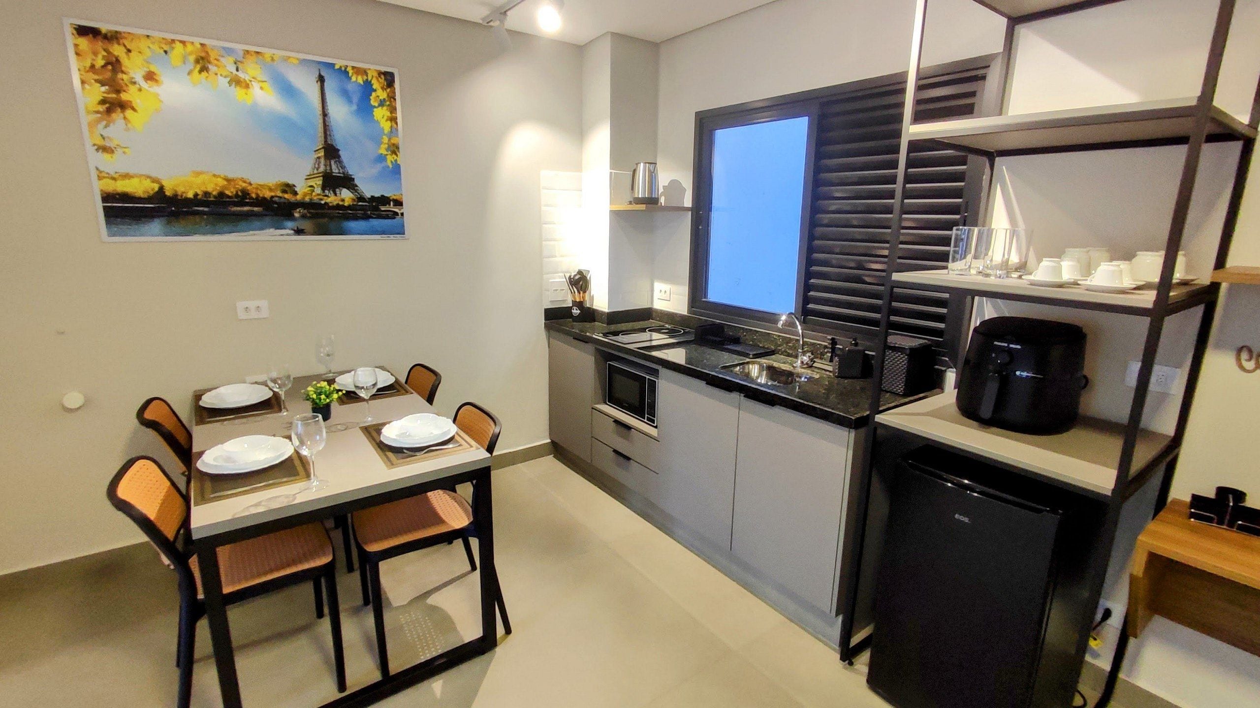 A compact kitchen with a dining area, a refrigerator, and a window with blinds.