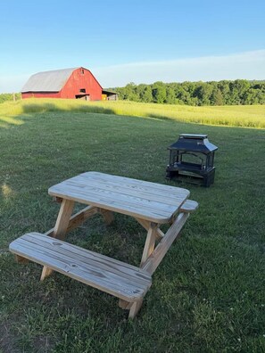 Una mesa de picnic con bancos en un campo cubierto de césped, con un granero al fondo.