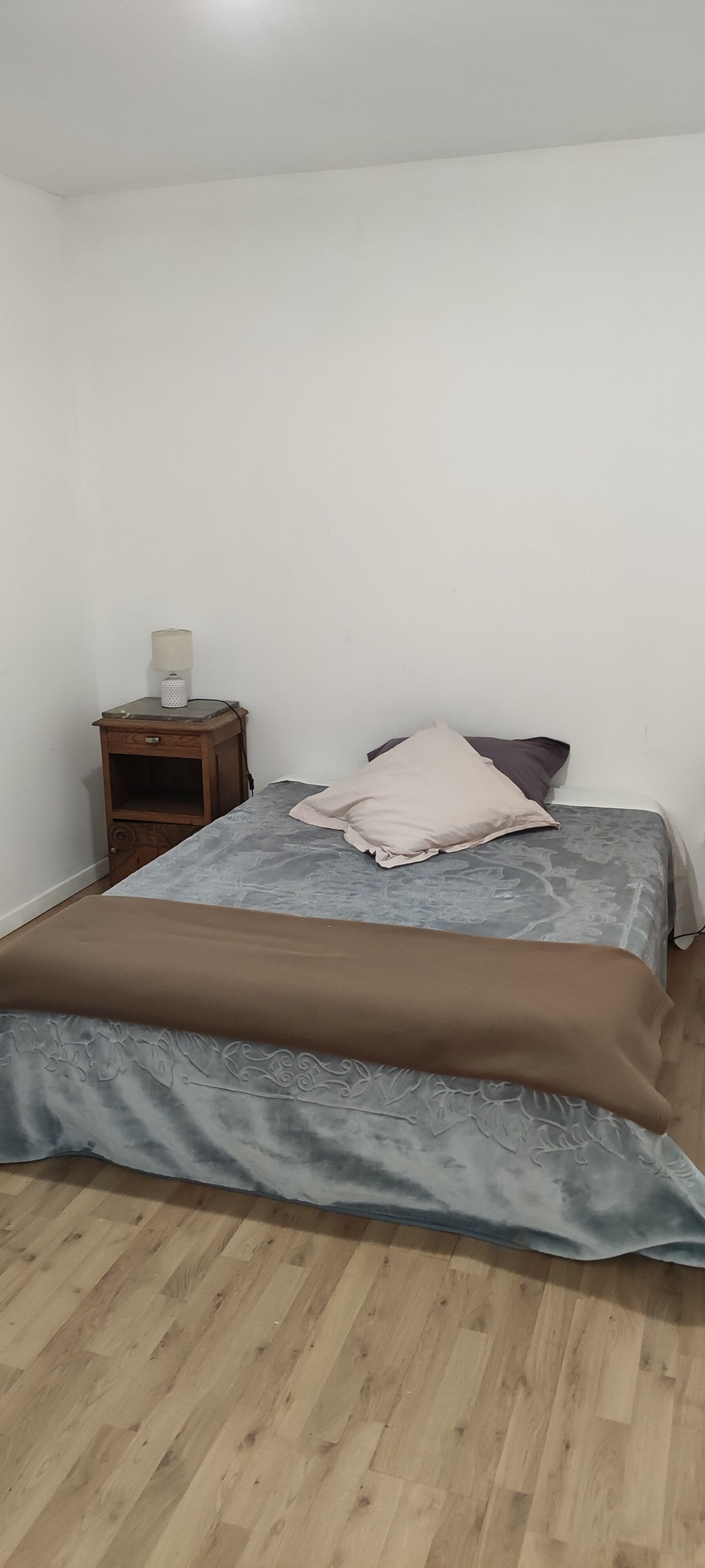 A bedroom with a bed, a nightstand, a lamp, and a wooden floor.