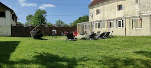 A grassy backyard with a wooden fence, a barbecue grill, and several lounge chairs. - Country house less than 1 hour from Paris and Reims, accommodates up to 30 people (Verdelot)