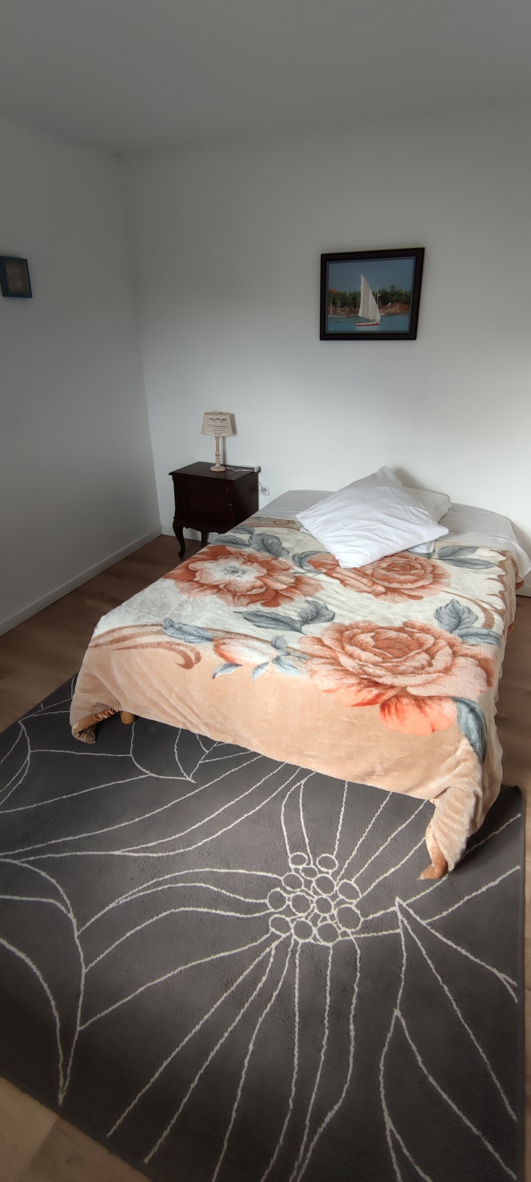Een slaapkamer met een bed, nachtkastje, een lijst met foto aan de muur en een kamerkleed met dessin.