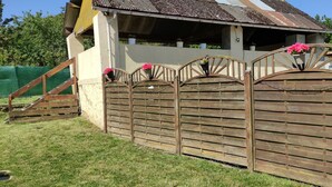 Une clôture en bois avec un portail, une maison avec un toit en tôle ondulée et, au fond, une autre clôture, cette fois-ci verte.