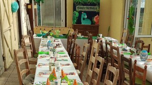 Une longue table à manger, décorée de chapeaux de fête, d’assiettes et de gobelets, placée sous une zone abritée et ornée d’une banderole d’anniversaire.