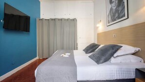 A bedroom with a bed, a curtain, a wall-mounted TV, and a framed picture.